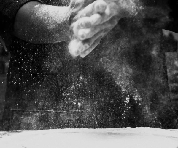 Black and white photo of a chef clapping flour in a kitchen, creating a dramatic effect.