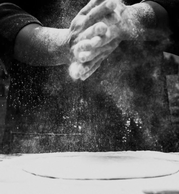 Black and white photo of a chef clapping flour in a kitchen, creating a dramatic effect.